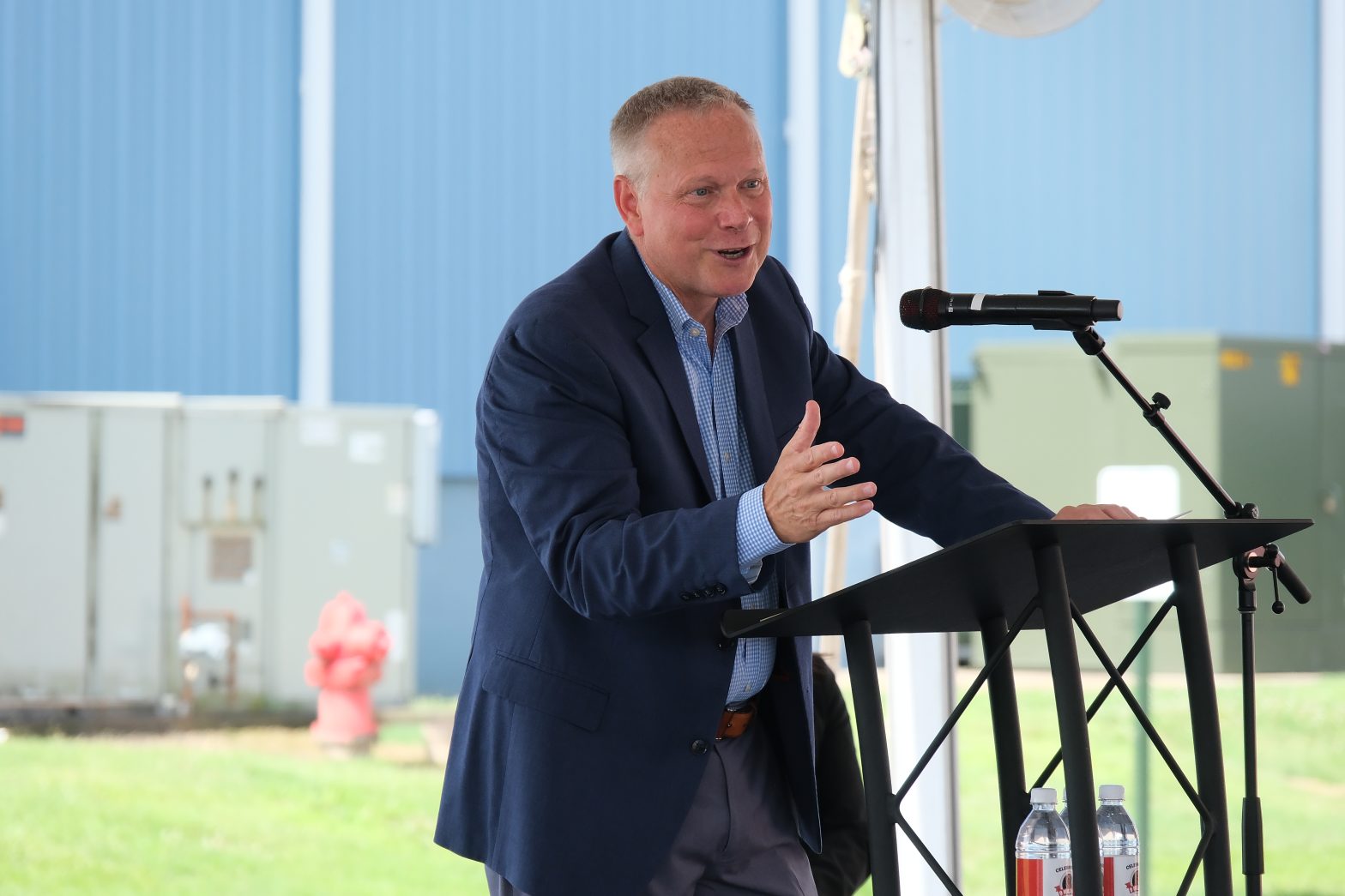 CEO TIm Mills delivering a speech at a podium, celebrating the 9 millionth transformer milestone in a decorated factory setting.
