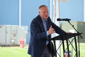 CEO TIm Mills delivering a speech at a podium, celebrating the 9 millionth transformer milestone in a decorated factory setting.