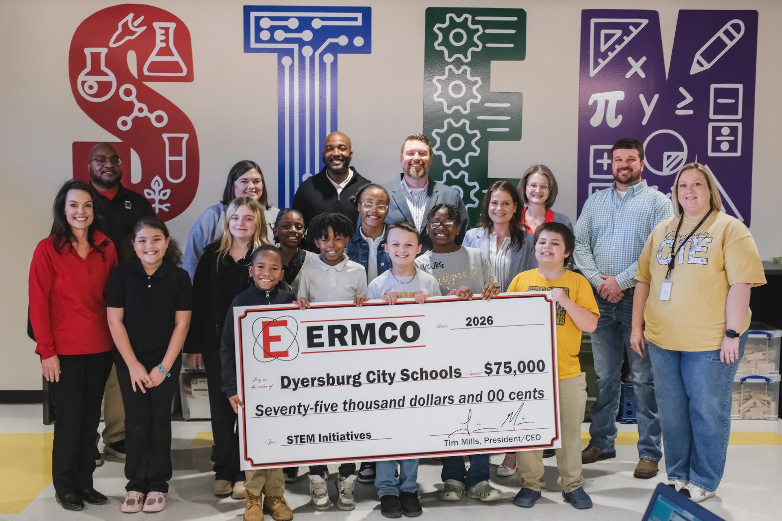 Group of ERMCO representatives, students, and Dyersburg City Schools staff displaying a ceremonial $75,000 STEM initiatives donation check in front of a colorful STEM?themed wall.