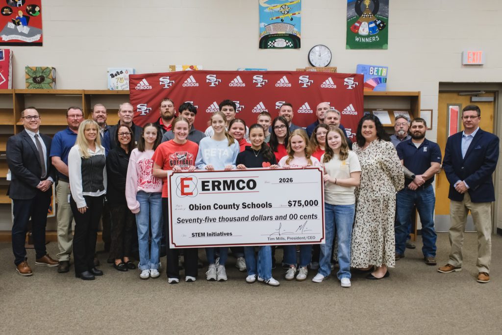 ERMCO team members and Obion County Schools students and staff standing together with a large $75,000 STEM initiatives donation check in a school media center.